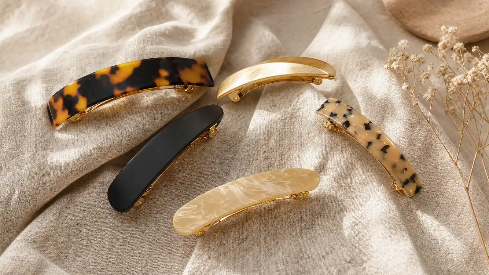 Tortoiseshell French hair barrette with an open metal clasp resting on linen beside a loose twist of brown hair