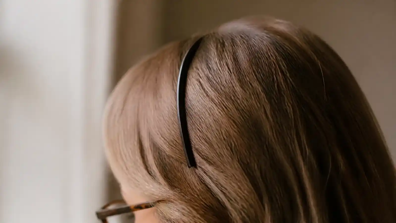 A slim dark headband crossing light brown hair and ending above the arm of a pair of tortoiseshell glasses, with a visible gap between the two