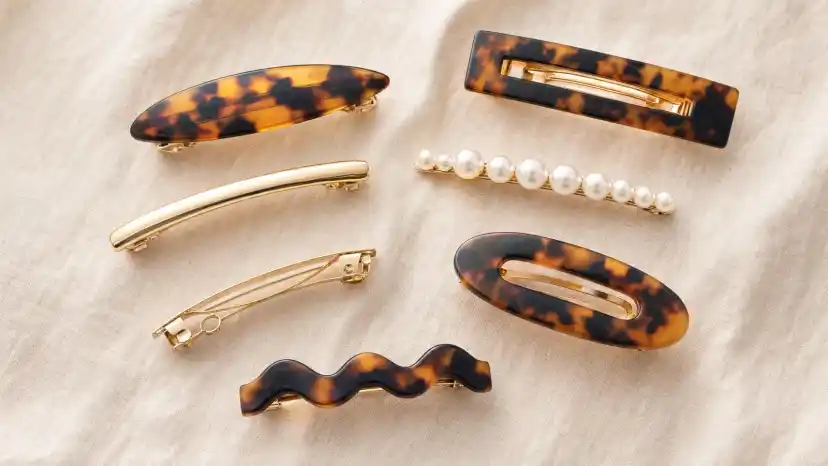 An assortment of hair barrettes including tortoiseshell, gold, pearl, and French styles arranged on cream linen