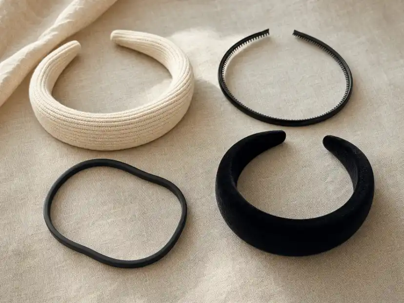 Four headband types laid out on linen: a wide ribbed-knit padded band, a slim toothed plastic band, a flexible bendable band and a black velvet padded band